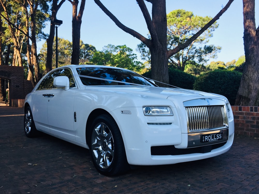a white rolls royce parked in front of some trees
