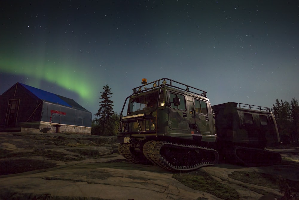 Un veicolo militare parcheggiato davanti a un fienile sotto l'aurora boreale