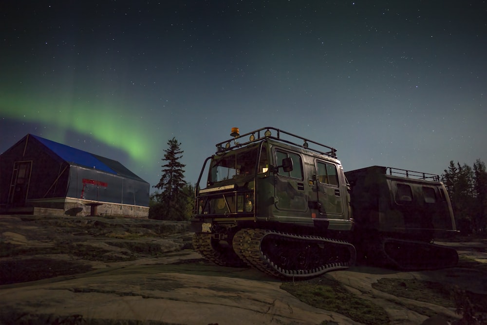 a military vehicle parked in front of a barn under the northern lights