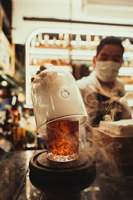 A bartender pouring a smoky whiskey cocktail into a chilled glass with ice cubes.