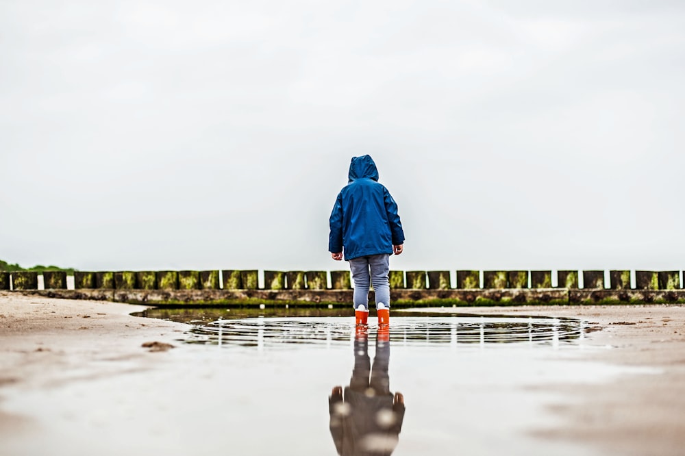 a person in a blue jacket is standing in a puddle
