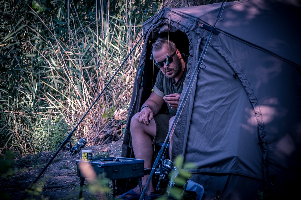 a man sitting inside of a tent next to a forest