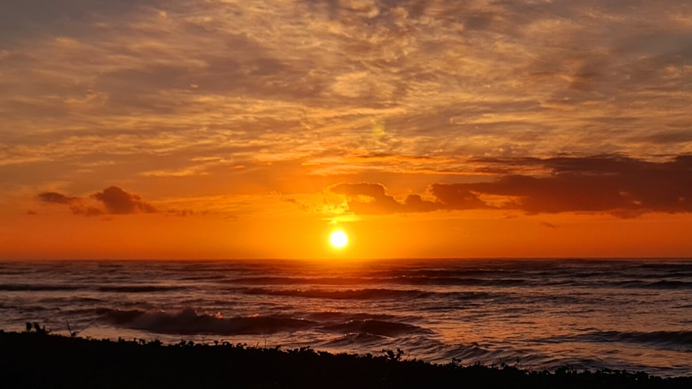 the sun is setting over the ocean on a cloudy day