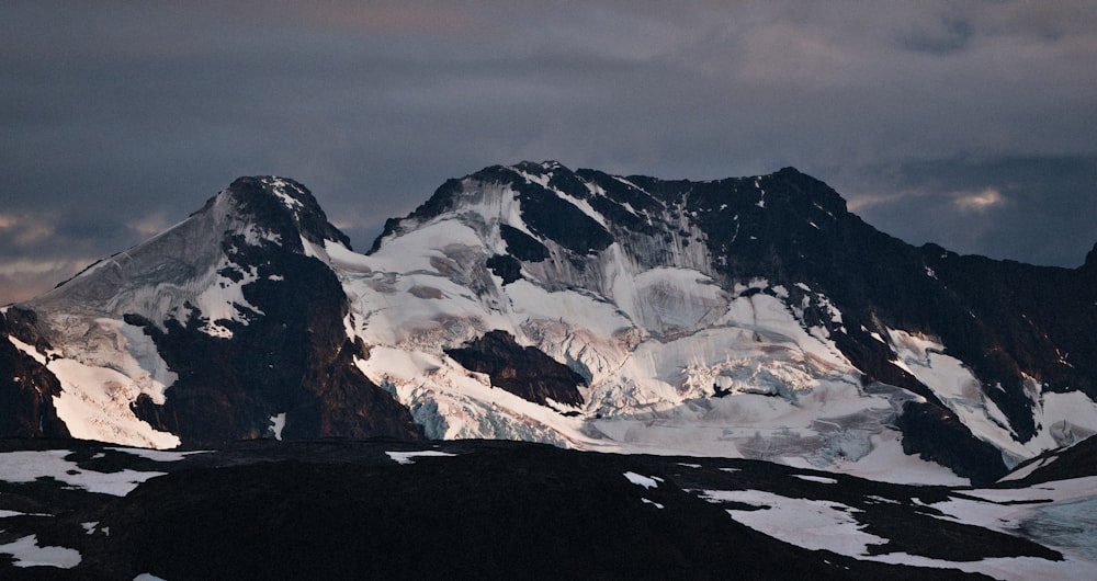 a mountain range covered in snow under a cloudy sky