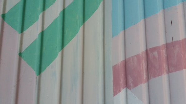A metal surface with diagonal green and pink stripes painted over ribbed panels. The paint is slightly worn, giving a rustic appearance.
