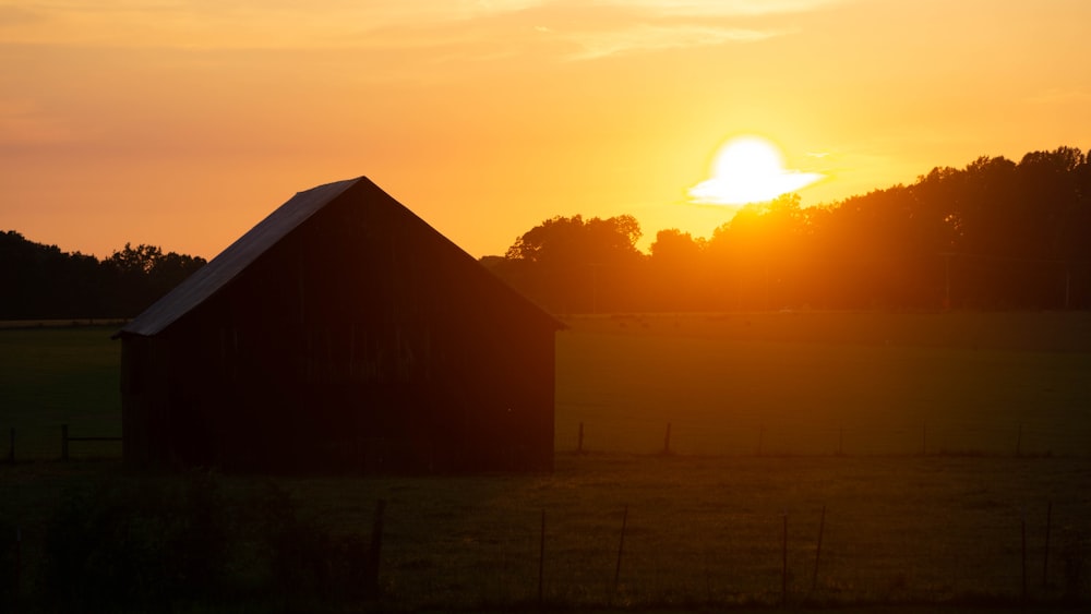 the sun is setting behind a barn in a field