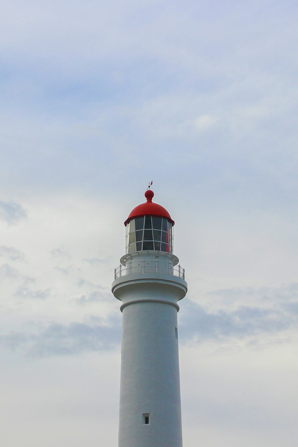 a white lighthouse with a red top on a cloudy day
