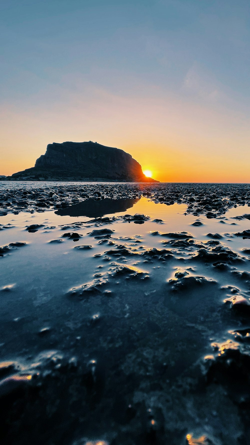 the sun is setting over a rocky beach