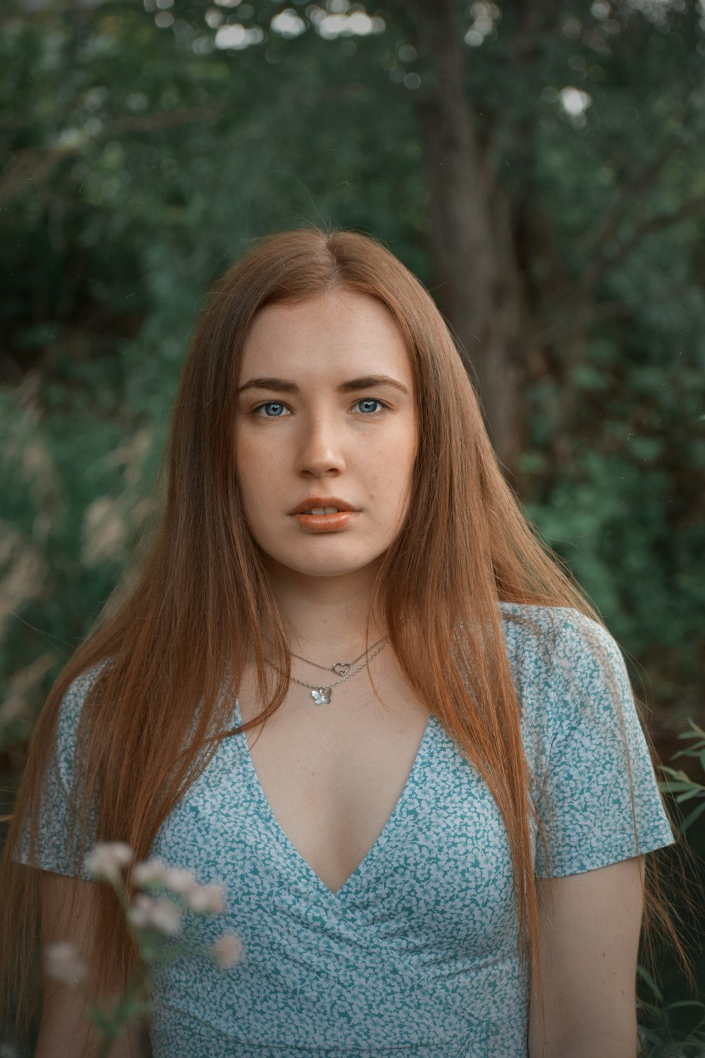 a woman with long red hair standing in a forest