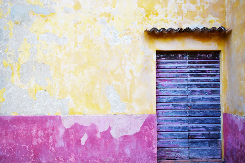 Un bâtiment jaune et rose avec une porte bleue