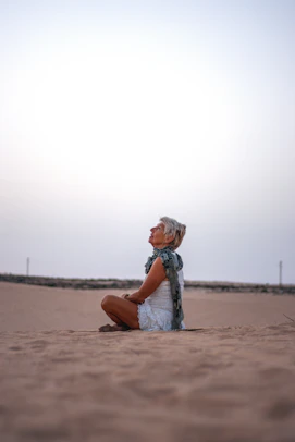 a woman sitting on the ground in the sand