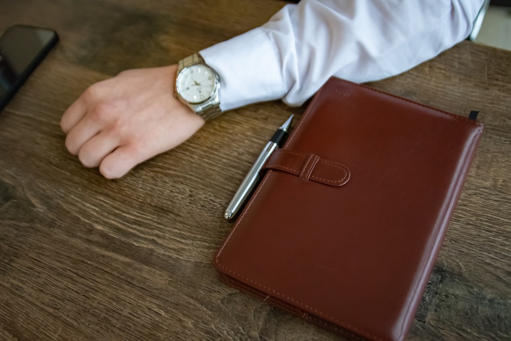 a person's hand with a watch on their wrist next to a brown leather