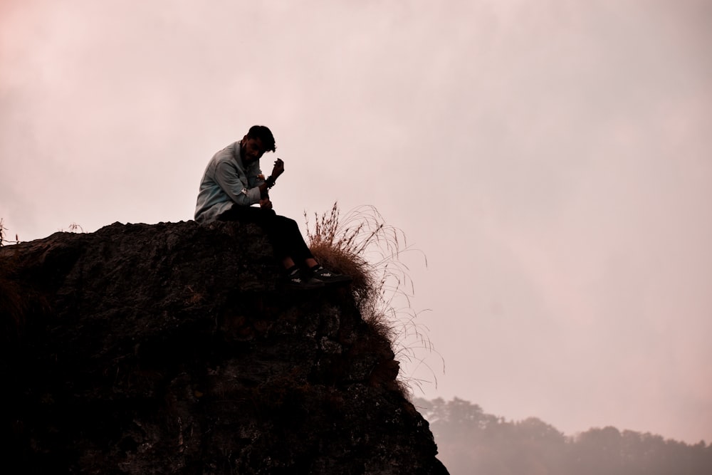 a man sitting on top of a rock next to a grass covered hillside