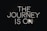 Neon lettering spells out 'The Journey is On' against a dark background, creating a bold and striking visual effect.