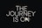 Neon lettering spells out 'The Journey is On' against a dark background, creating a bold and striking visual effect.