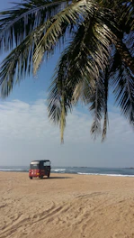 A cheerful tuk tuk parked by the turquoise sea with lush green hills in the background.