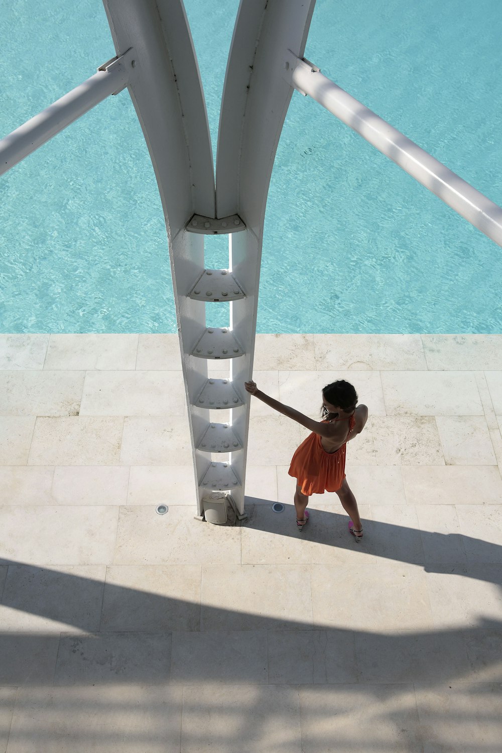 a little girl holding onto a pole next to a pool