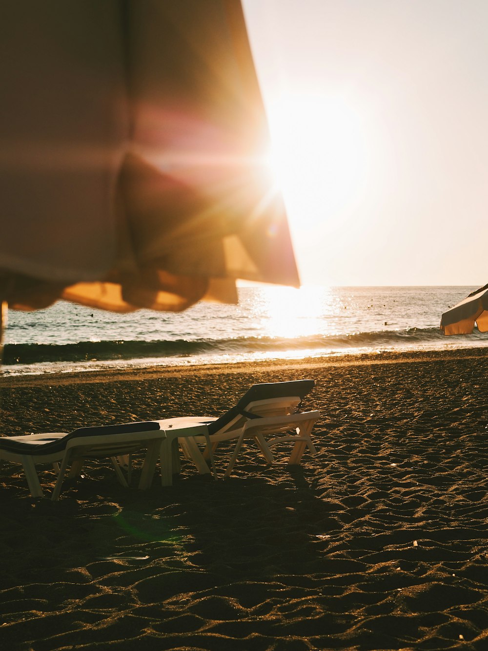 the sun is setting on the beach with chairs and umbrellas