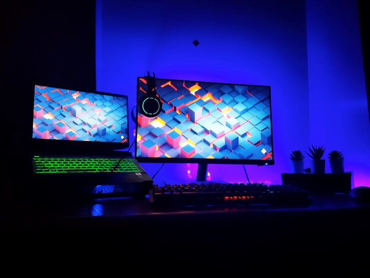 Dual gaming monitors on a desk in a low-light room