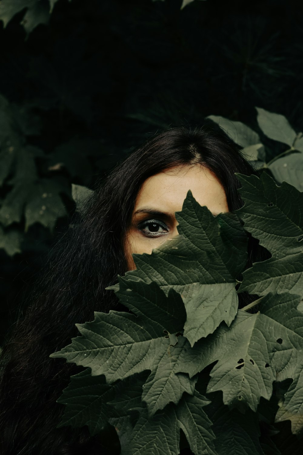 Eine Frau, die sich mit weit geöffneten Augen hinter Blättern versteckt