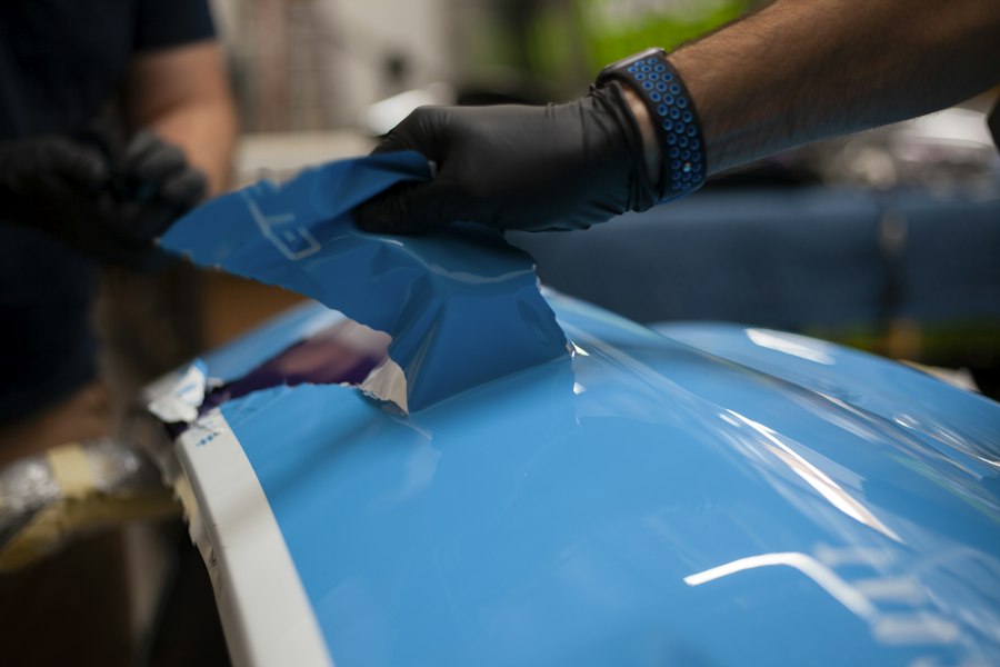 Technician applying vinyl wrap film to a vehicle panel