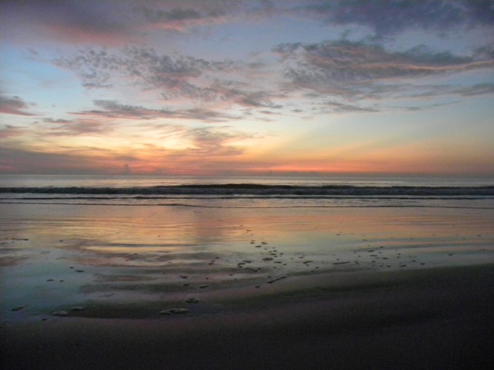 the sun is setting over the water at the beach