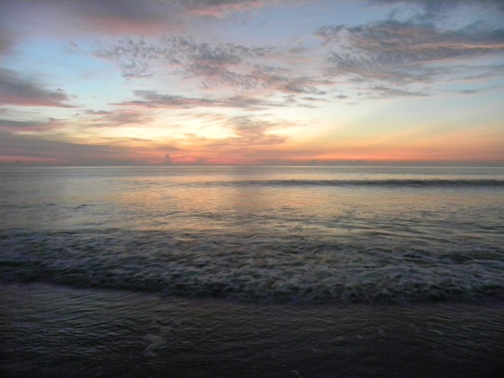 the sun is setting over the water at the beach