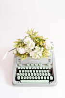 A vintage typewriter with a fresh page, surrounded by dried flowers in shades of pink and violet.