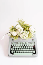 Soft lavender and blush peach floral arrangement beside a vintage typewriter on a milky cream background.