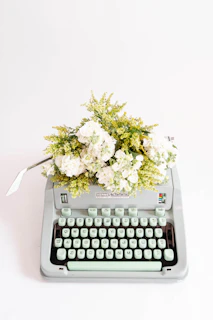 A vintage typewriter with a fresh page, surrounded by dried flowers in shades of pink and violet.