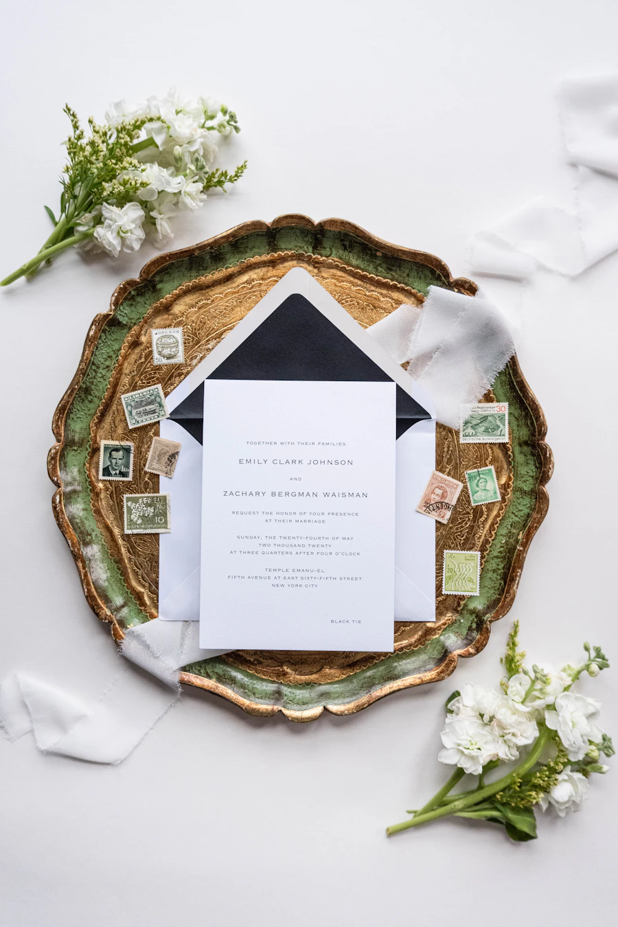 Black and white wedding invitation stationery and envelopes arranged on a tray with white flowers