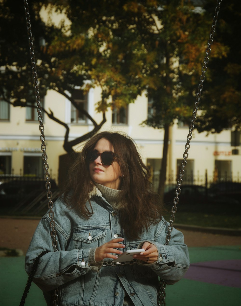 a woman wearing sunglasses and a denim jacket on a swing