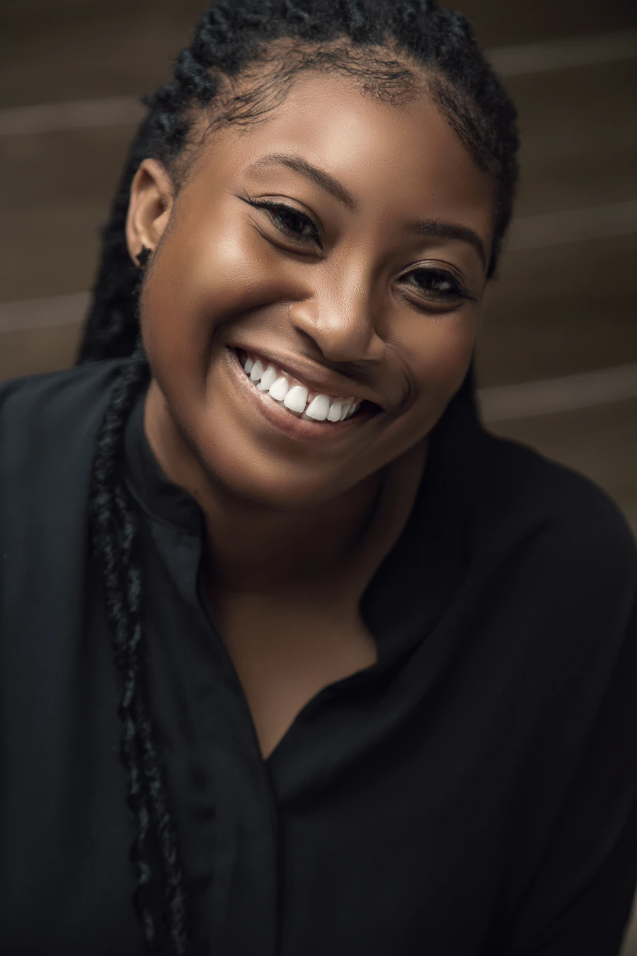 Portrait souriant d'une femme aux cheveux tressés, chemise noire, photographié à Accra.