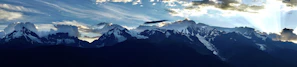 A panoramic view of a mountain range under a dramatic sky, seen on a hiking trip.