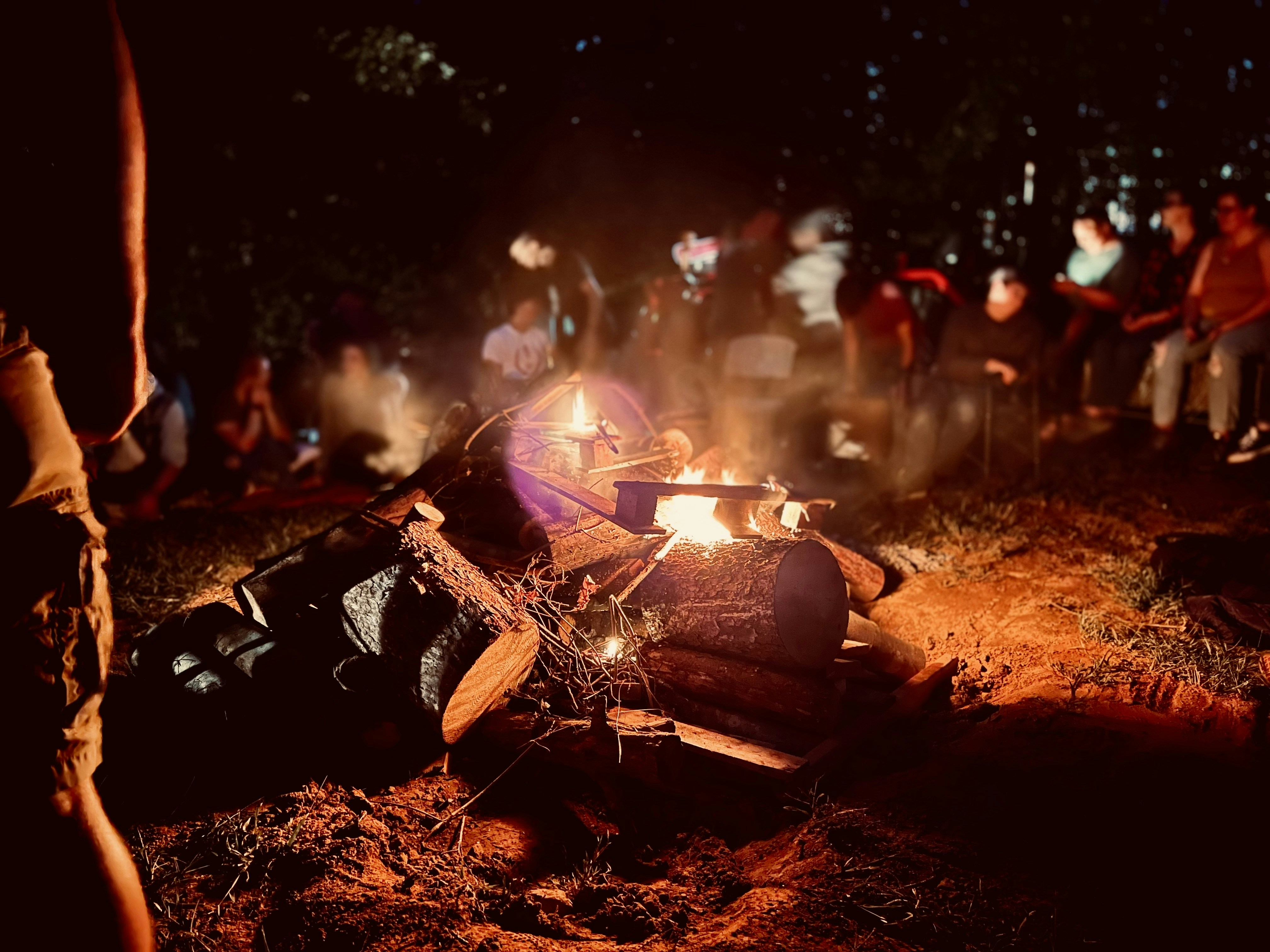 Evening campfire gathering in forest, warm amber light, people seated in circle, reflective atmosphere