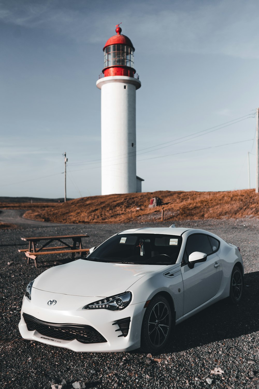 a white sports car parked in front of a lighthouse