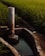 An irrigation system with a concrete water channel and a vertical pipe is set amid a lush, green field of rice plants. The sunlight casts warm tones over the vegetation.
