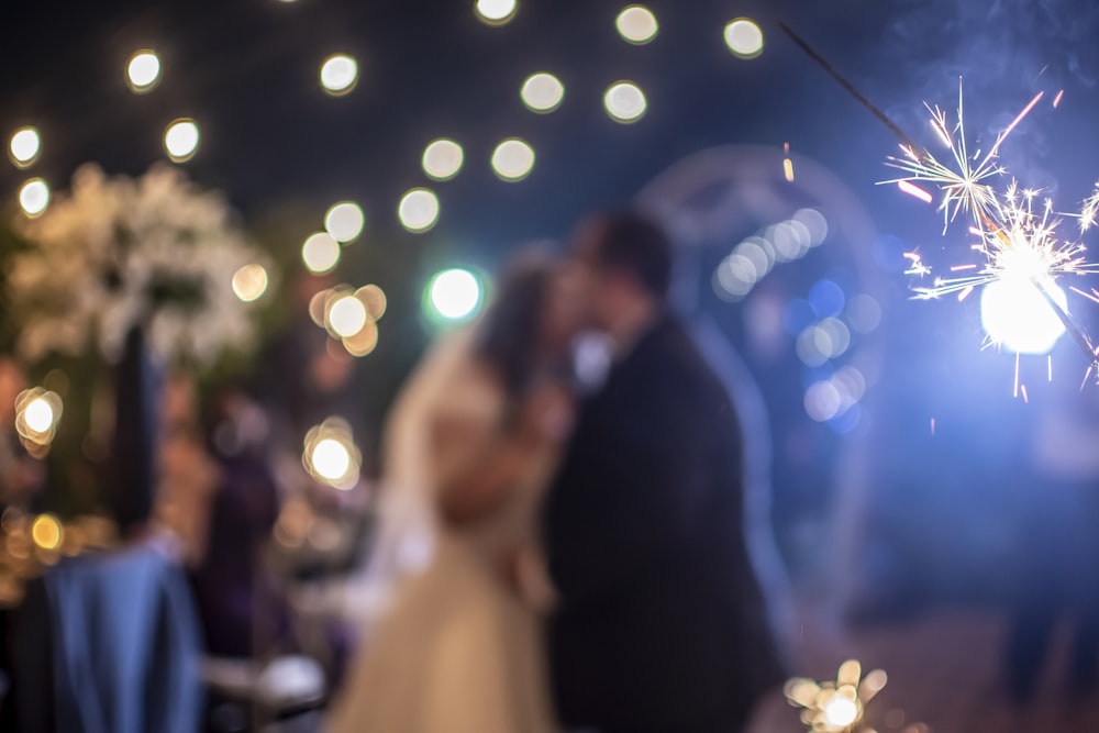 Una novia y un novio besándose frente a fuegos artificiales