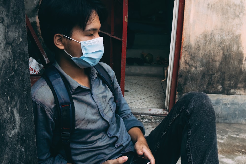 a man sitting on the ground wearing a face mask