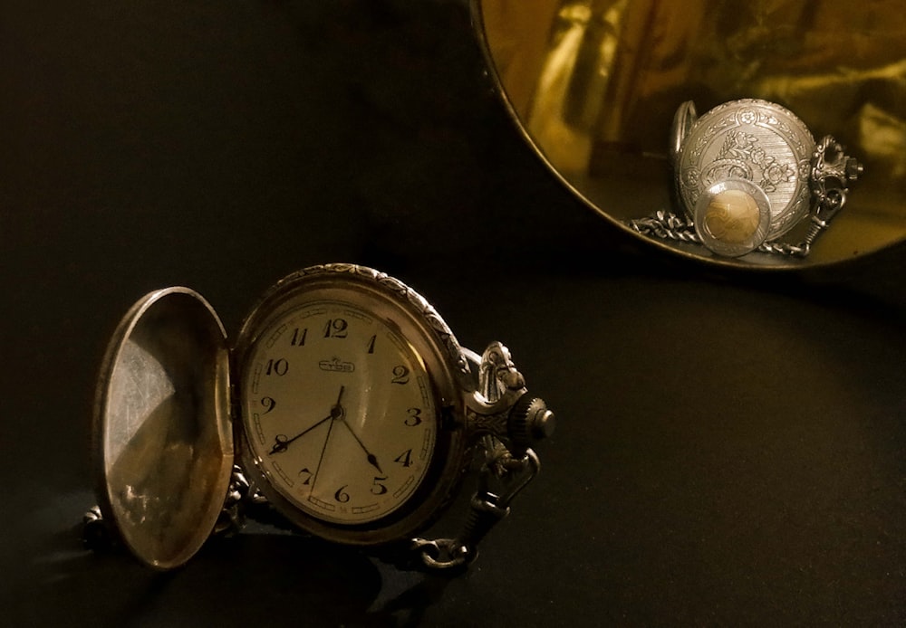 an antique pocket watch sitting next to a mirror