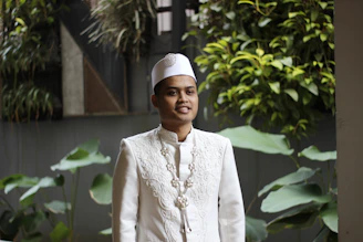 a man in a white outfit standing in front of some plants