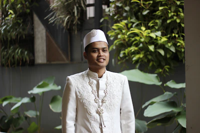 a man in a white outfit standing in front of some plants