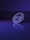 A detailed, intricate piece of jewelry is positioned on a reflective surface, illuminated by purple and blue lighting. The intricate patterns and symmetry are highlighted by the lighting, creating an elegant and captivating reflection.