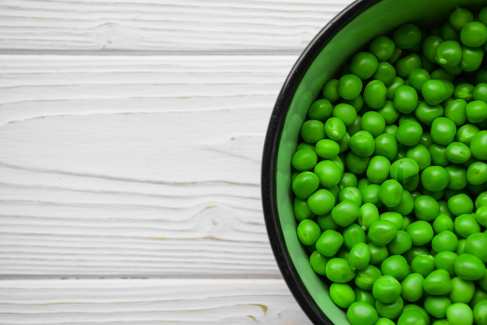 un bol vert rempli de petits pois sur une table blanche