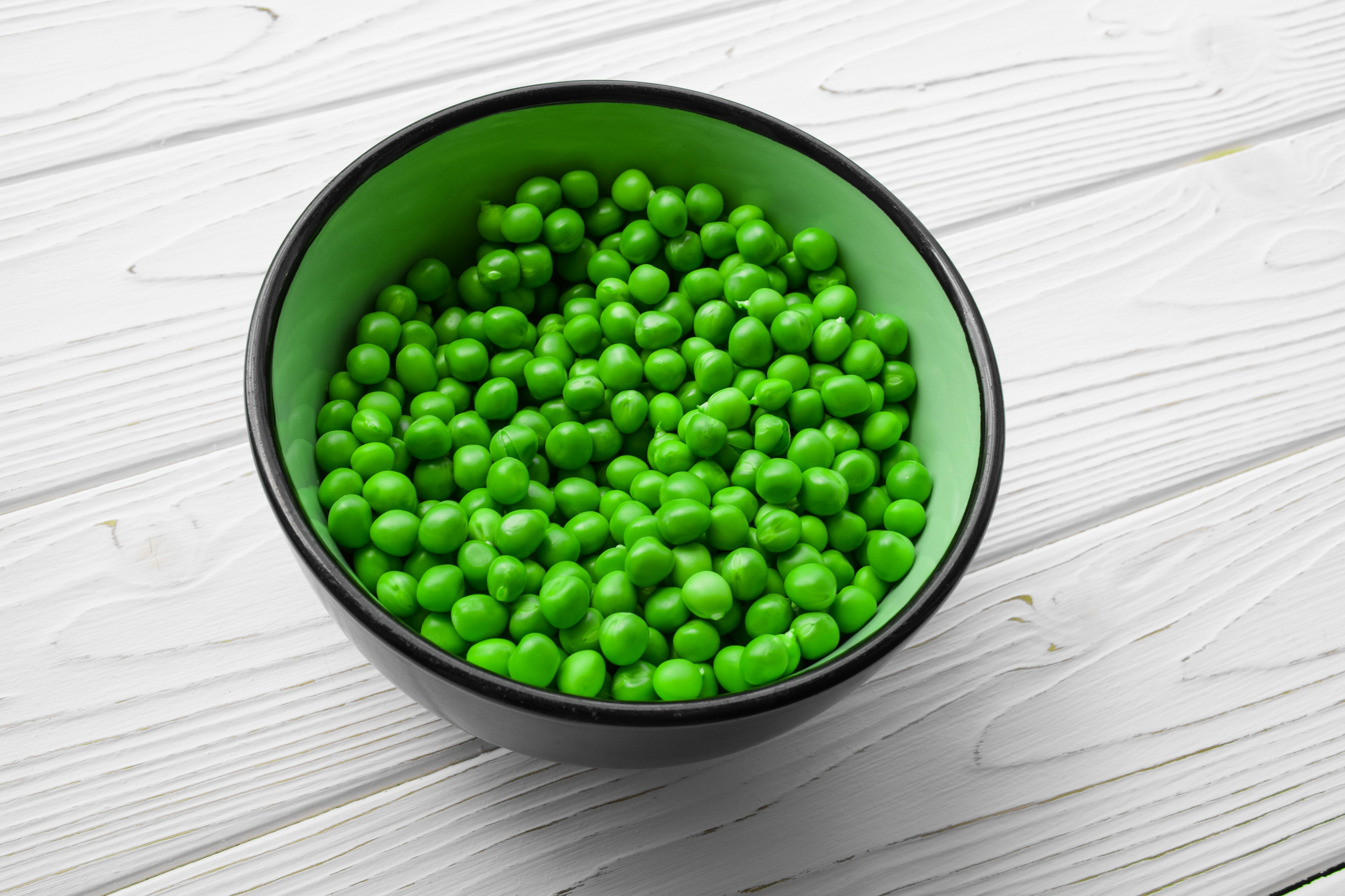 a green bowl filled with peas on top of a white table