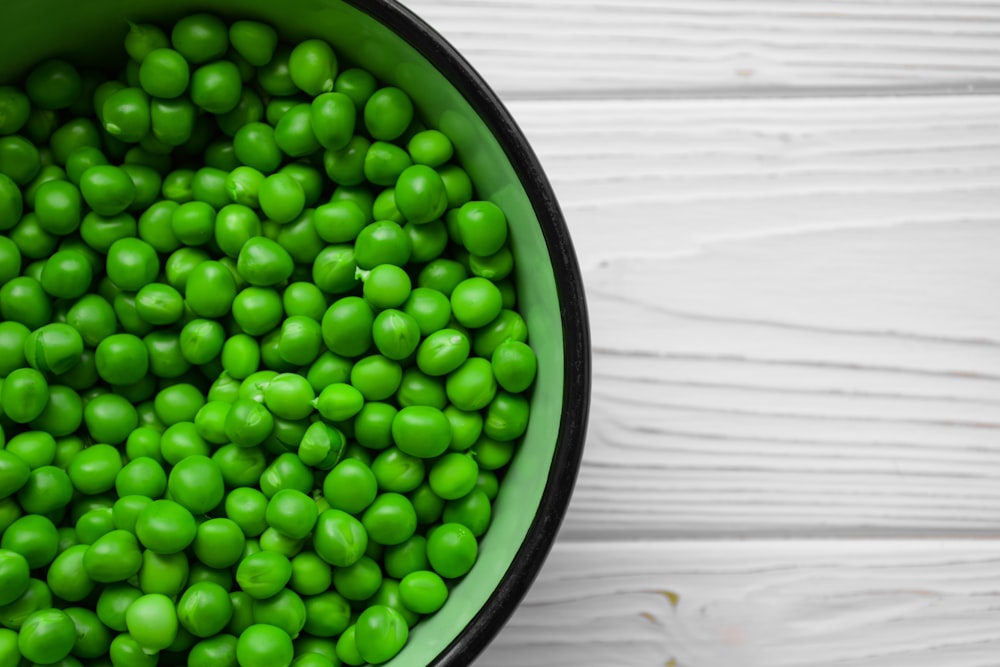 a green bowl filled with peas on top of a white table