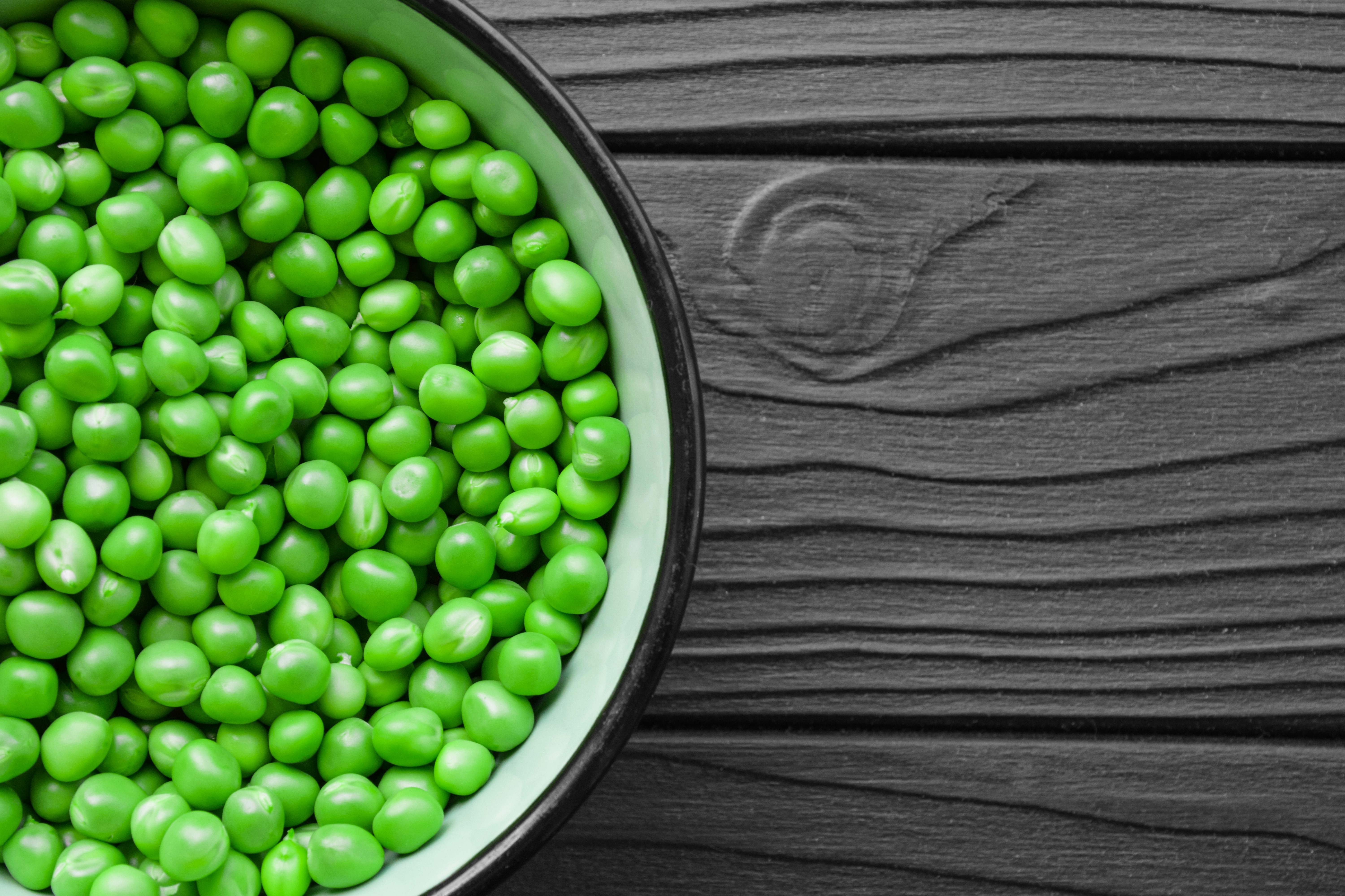 a bowl filled with green peas on top of a wooden table