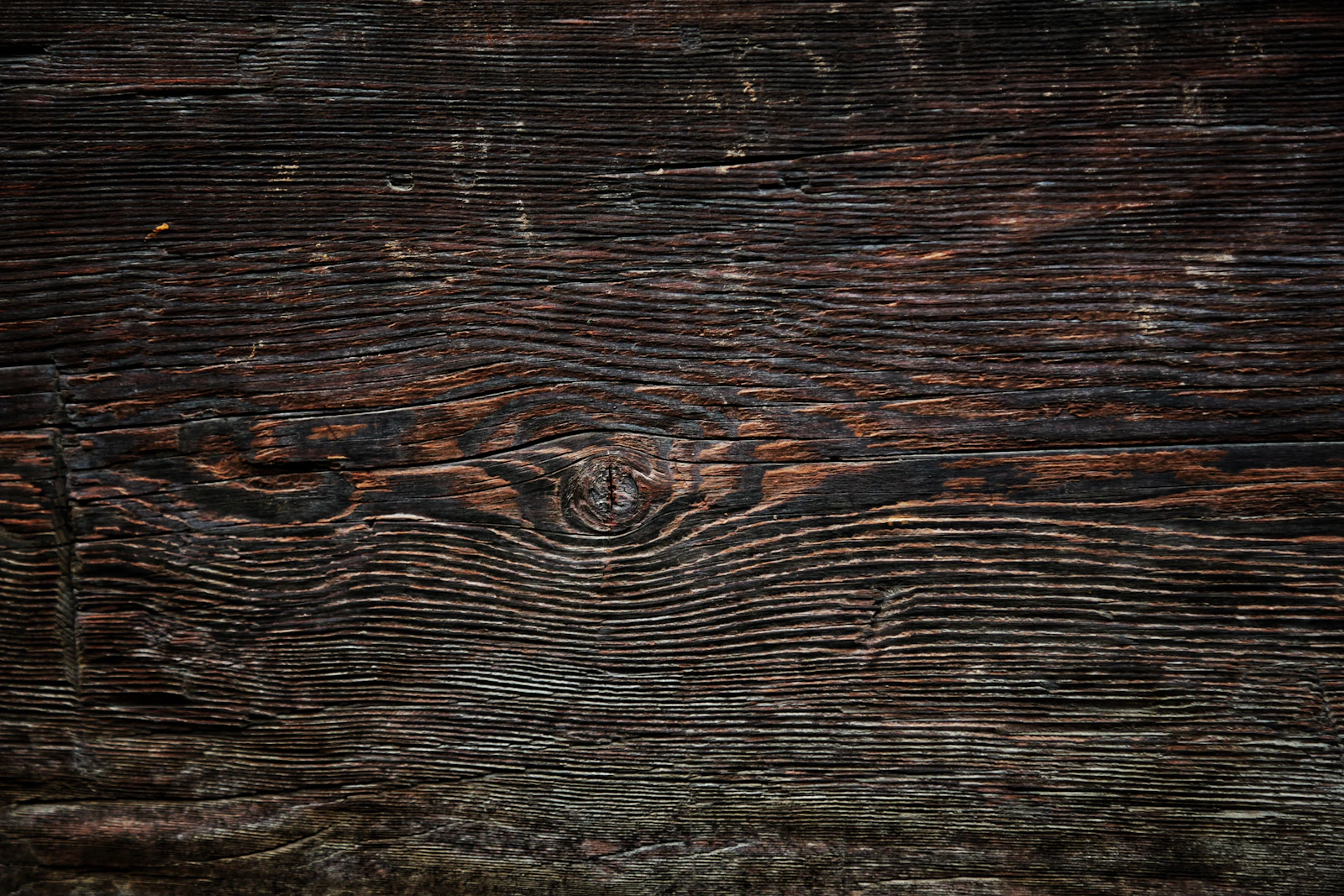Dark, weathered timber with a knot and long lines of grain running across it