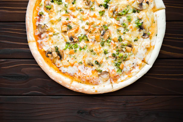 Freshly baked pizza topped with melty cheese, chicken supreme, and colorful veggies on a dark wooden table