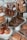 Assortment of baked goods displayed in a glass bakery case. Large glass jars contain stacks of cookies, including chocolate and oatmeal raisin varieties. Muffins with raisins are placed on a plate in the foreground, while croissants and pastries are arranged on wooden boards.